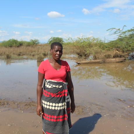 Esnert Thaison standing dejectedly in front of her submerged crop field.